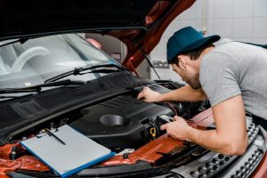auto electrician with multimeter voltmeter checking car battery voltage at mechanic's workshop